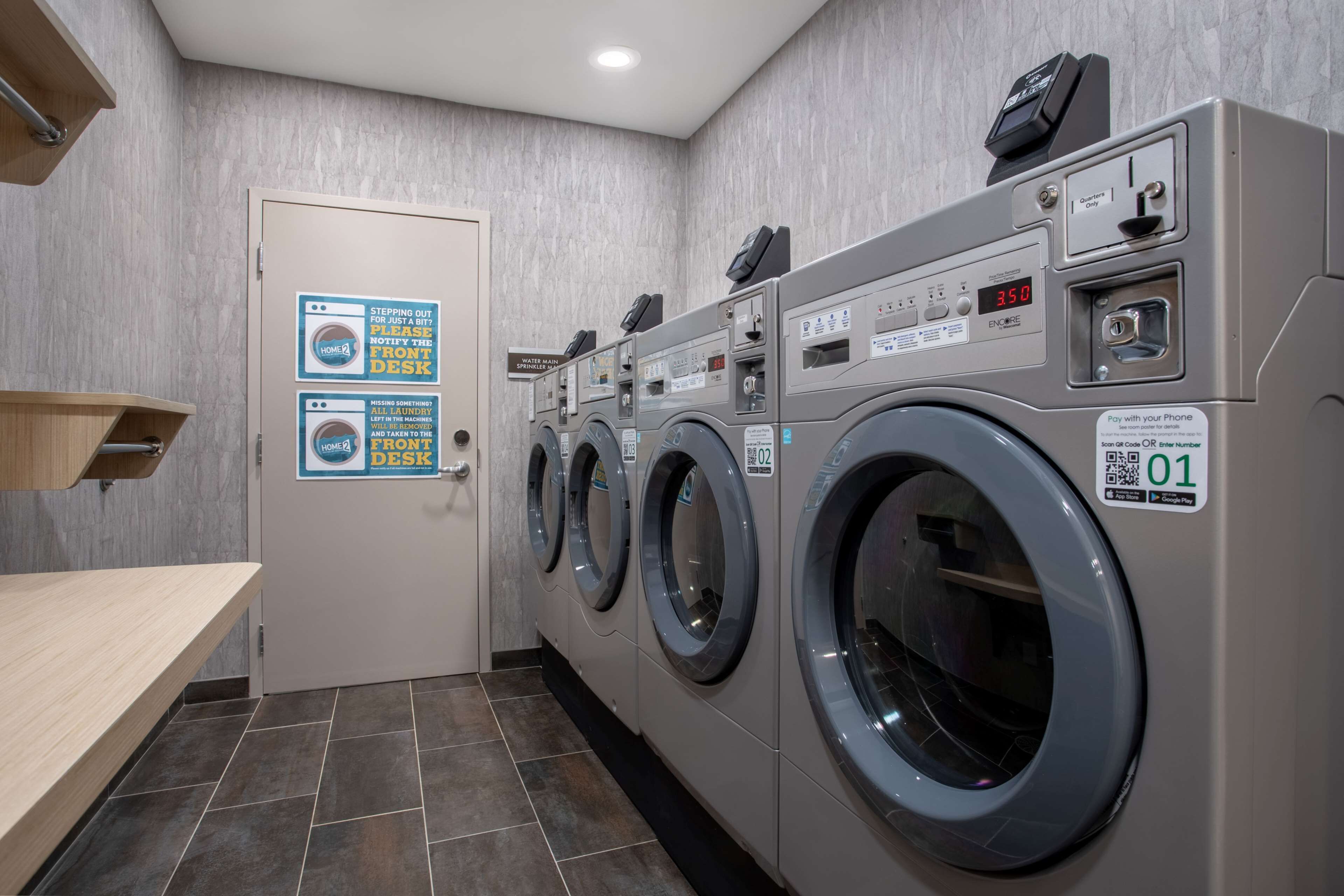 A laundry facility with multiple washing machines, a front desk, and a sign indicating the cost of using the machines.