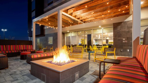 An outdoor seating area with a fire feature, yellow chairs, and a modern building in the background. - Home2 Suites By Hilton Calhoun (Calhoun)