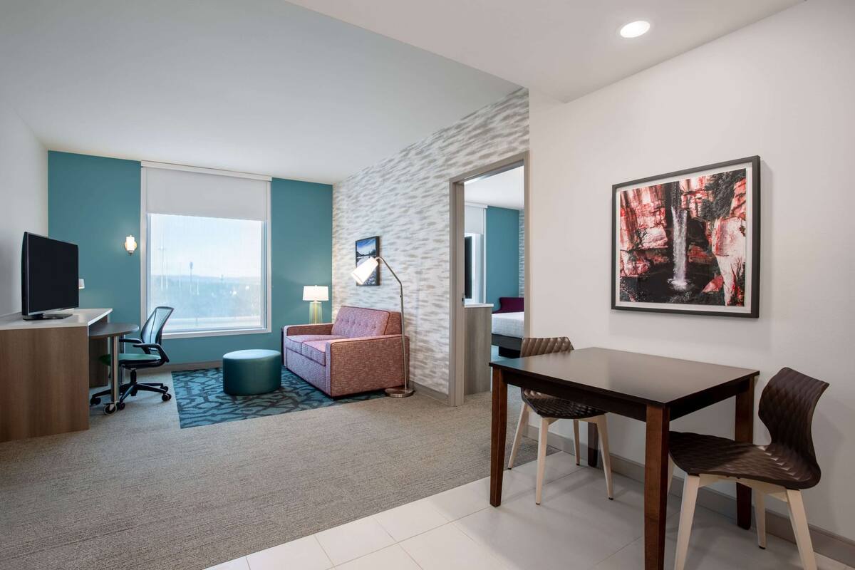 Una habitación de hotel moderna con escritorio, silla, sofá y mesa de comedor.