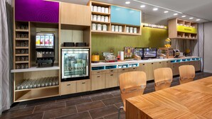 A modern breakfast bar with a refrigerator, shelves with glassware, and a seating area with wooden chairs. - Home2 Suites By Hilton Calhoun (Calhoun)