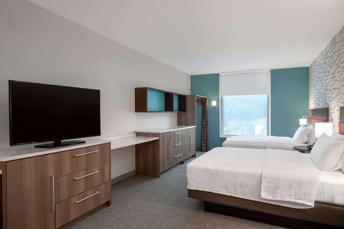 Una habitación de hotel moderna con televisión de pantalla plana, escritorio, cama con ropa blanca y ventana con cortinas.