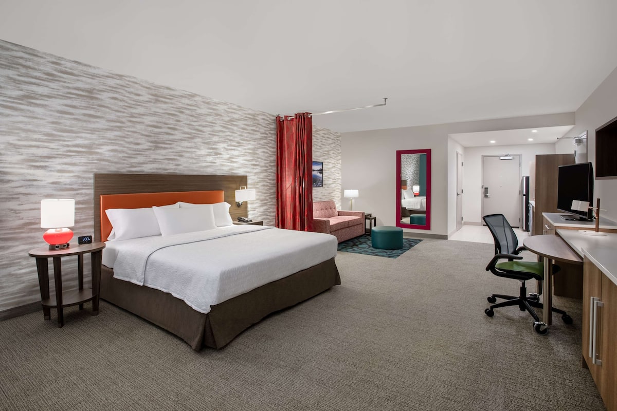 Habitación de hotel con una cama grande, un escritorio con silla, un televisor y un baño visible a través de una puerta abierta.