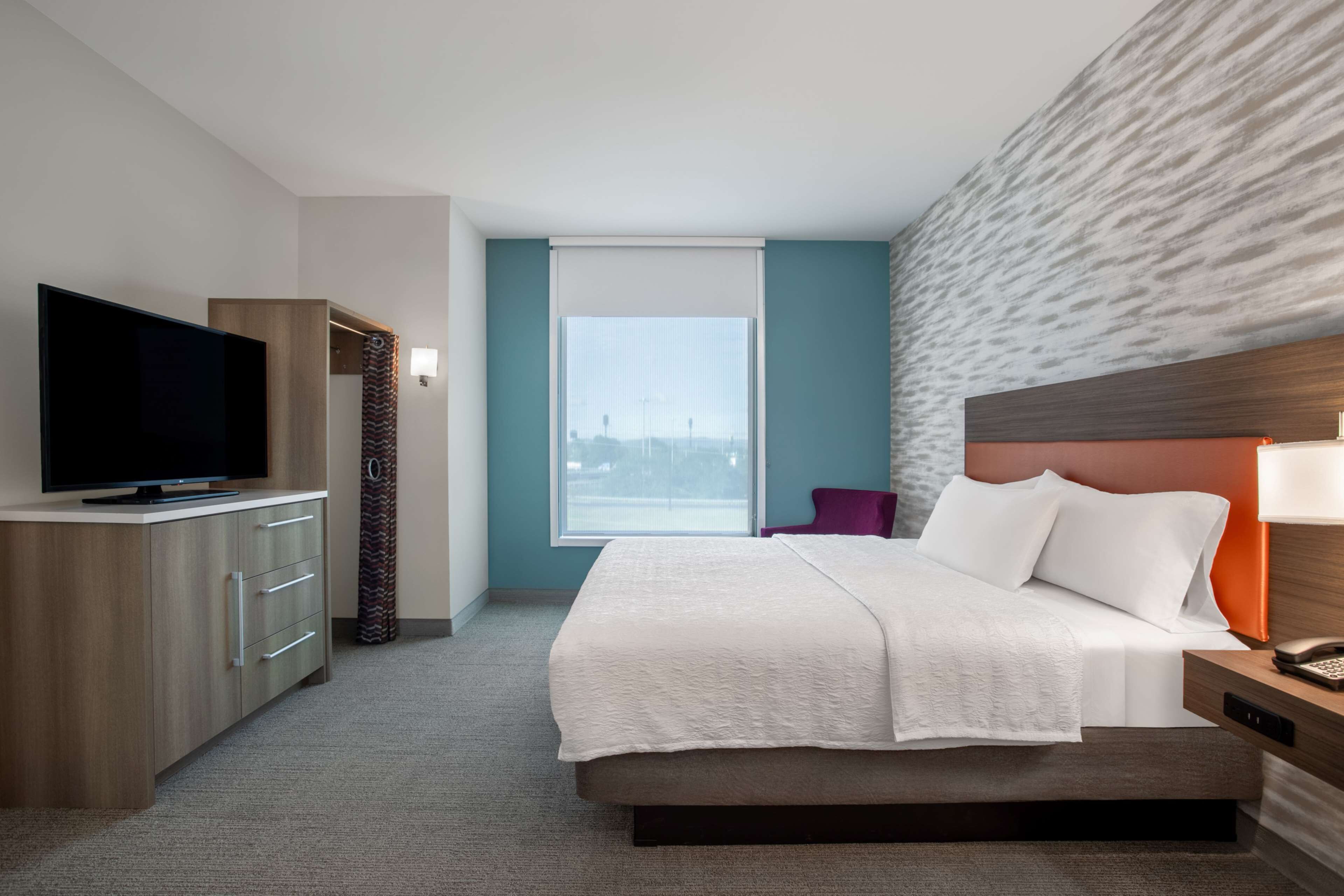 A hotel room with a bed, a TV, a desk, and a window with a view.