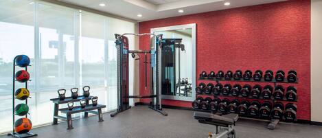 A gym with kettlebells, dumbbells, a bench, and a squat rack.
