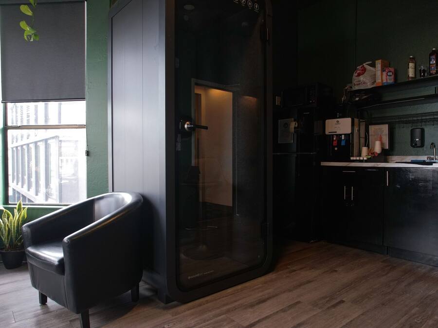 A modern kitchen with a black chair, a glass door, and a view of the street outside.