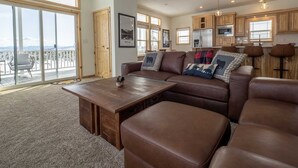 A spacious living area with a large sofa, a wooden coffee table, and a view of the outdoors through large windows.