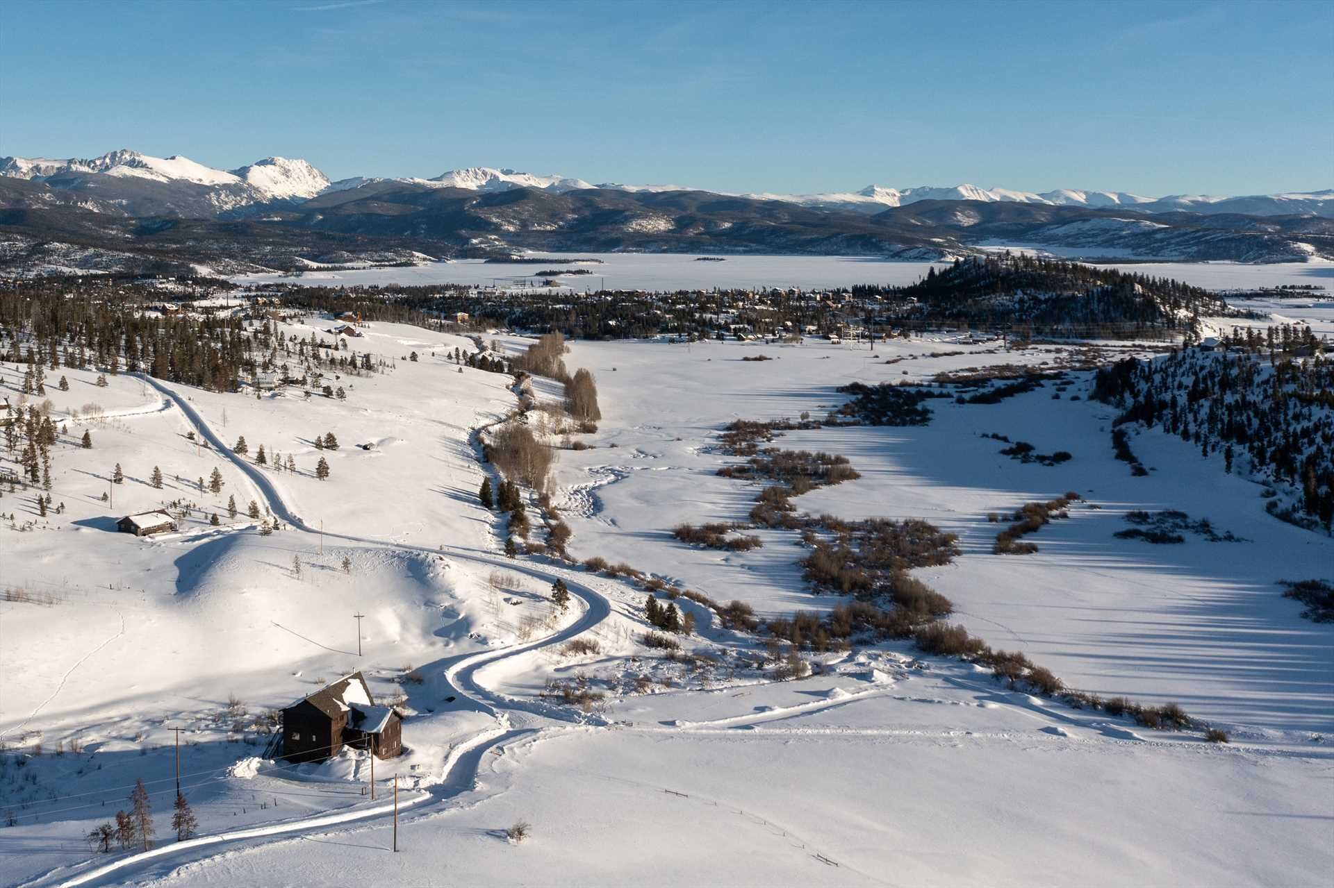 Paesaggio innevato con una strada tortuosa, un piccolo edificio e montagne in lontananza.