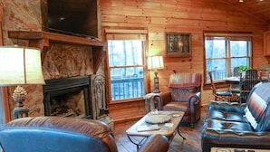 Un intérieur de chalet chaleureux avec une cheminée, des meubles en cuir et de grandes fenêtres.