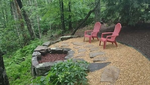 Une zone boisée avec un foyer en pierre et deux chaises Adirondack rouges.