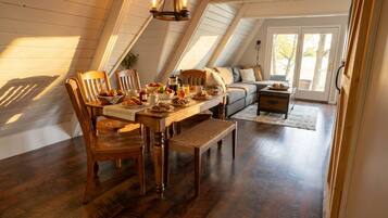 A cozy dining area with a wooden table set for breakfast, surrounded by chairs, in a room with sloped ceilings and a view through a glass door.