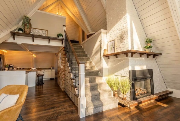 A spacious loft with a fireplace, wooden floors, and a kitchen area.