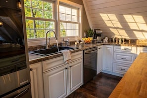 A kitchen with white cabinets, a granite countertop, a stainless steel sink, and a window with a view of trees.