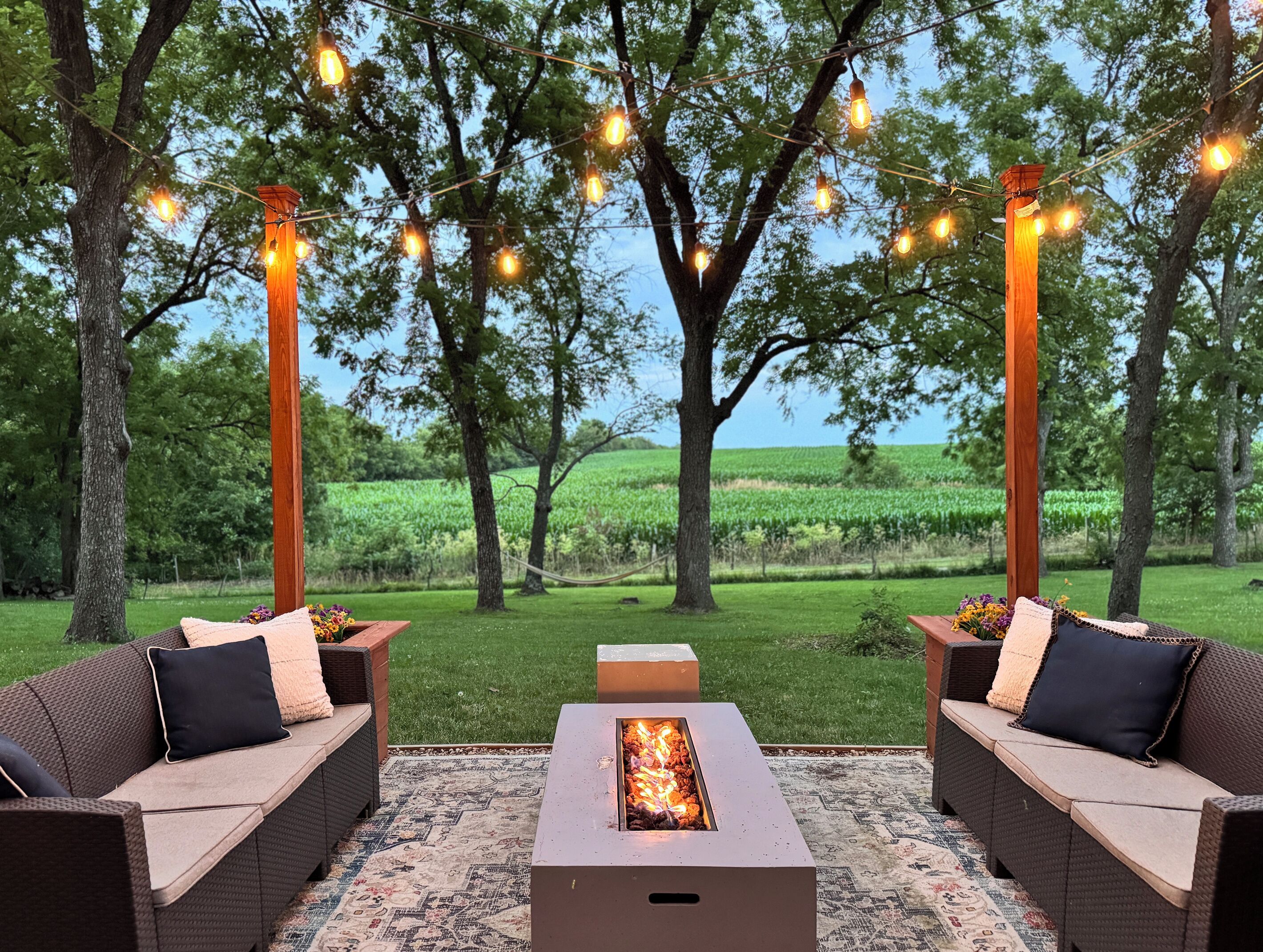 An outdoor seating area with two sofas, a fire pit, and string lights.