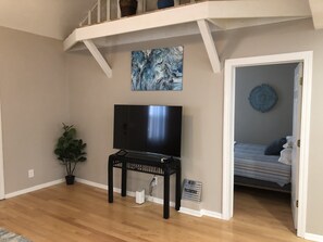 A living room with a TV on a stand, a plant, and a painting on the wall.