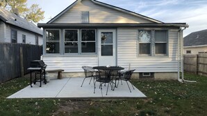 Una casa con un patio, una parrilla y una mesa con sillas.
