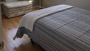 Un dormitorio con cama, una banca, una lámpara de pie y dos ventanas.