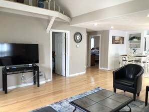 A spacious living room with a flat-screen TV, a coffee table, and a leather chair. There is a staircase leading to an upper level, and a dining area with a table and chairs. - Amy's Baby Blue is just steps from the Zoo (Omaha)