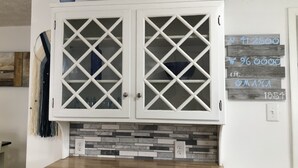 Una cocina con un armario blanco con puertas de vidrio con diseño de rombos, una encimera de madera y un salpicadero de mosaicos.