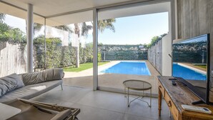 A modern living room with a pool view, a sofa, a table, and a TV. - Amazing home in Marina di Ragusa (Marina di Ragusa)