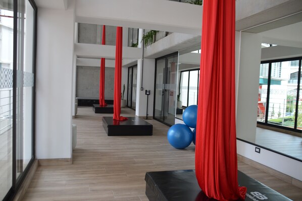 A modern gym with wooden floors, red exercise equipment, and large windows offering views of the outside.