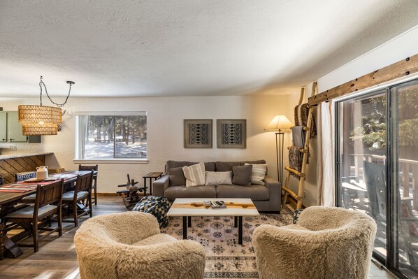 A cozy living room with a wooden dining table, a sofa, and fluffy chairs.