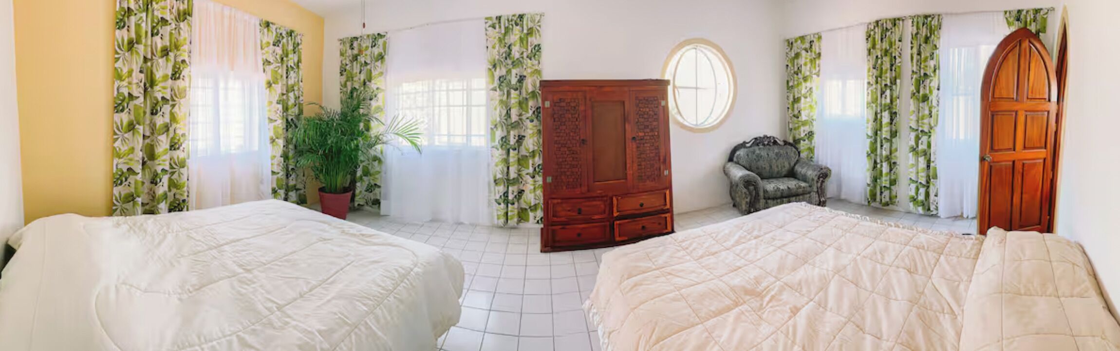 Une chambre avec deux lits, une armoire, une plante en pot et une fenêtre avec des rideaux.
