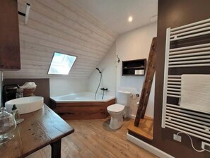Et badeværelse med træloft, badekar, toilet og et vindue.