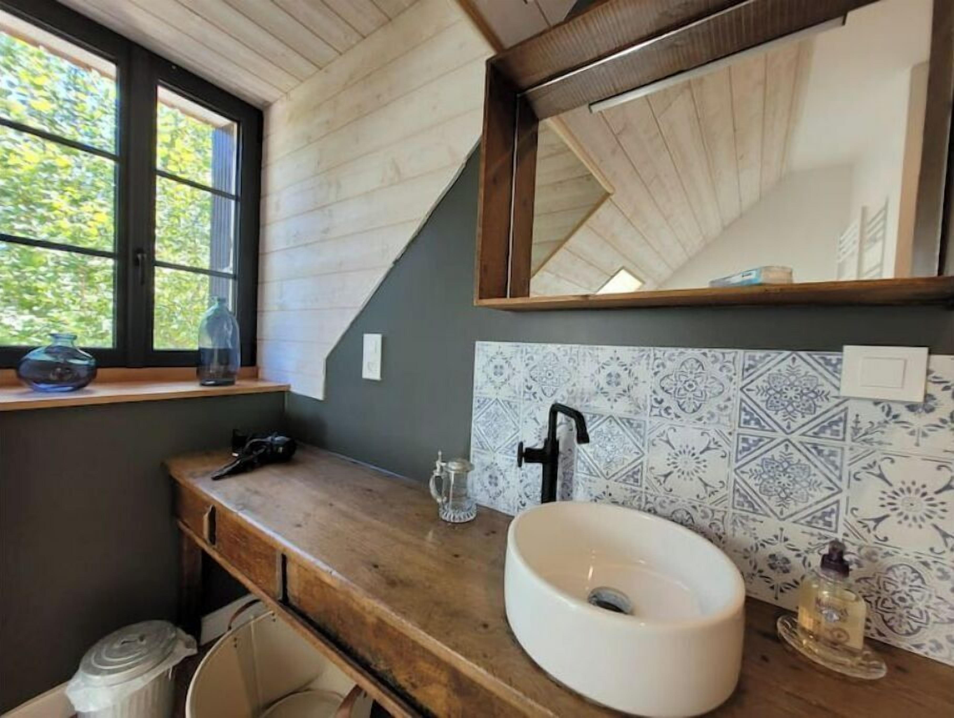 A bathroom with a wooden vanity, a white sink, a mirror, and patterned tiles.