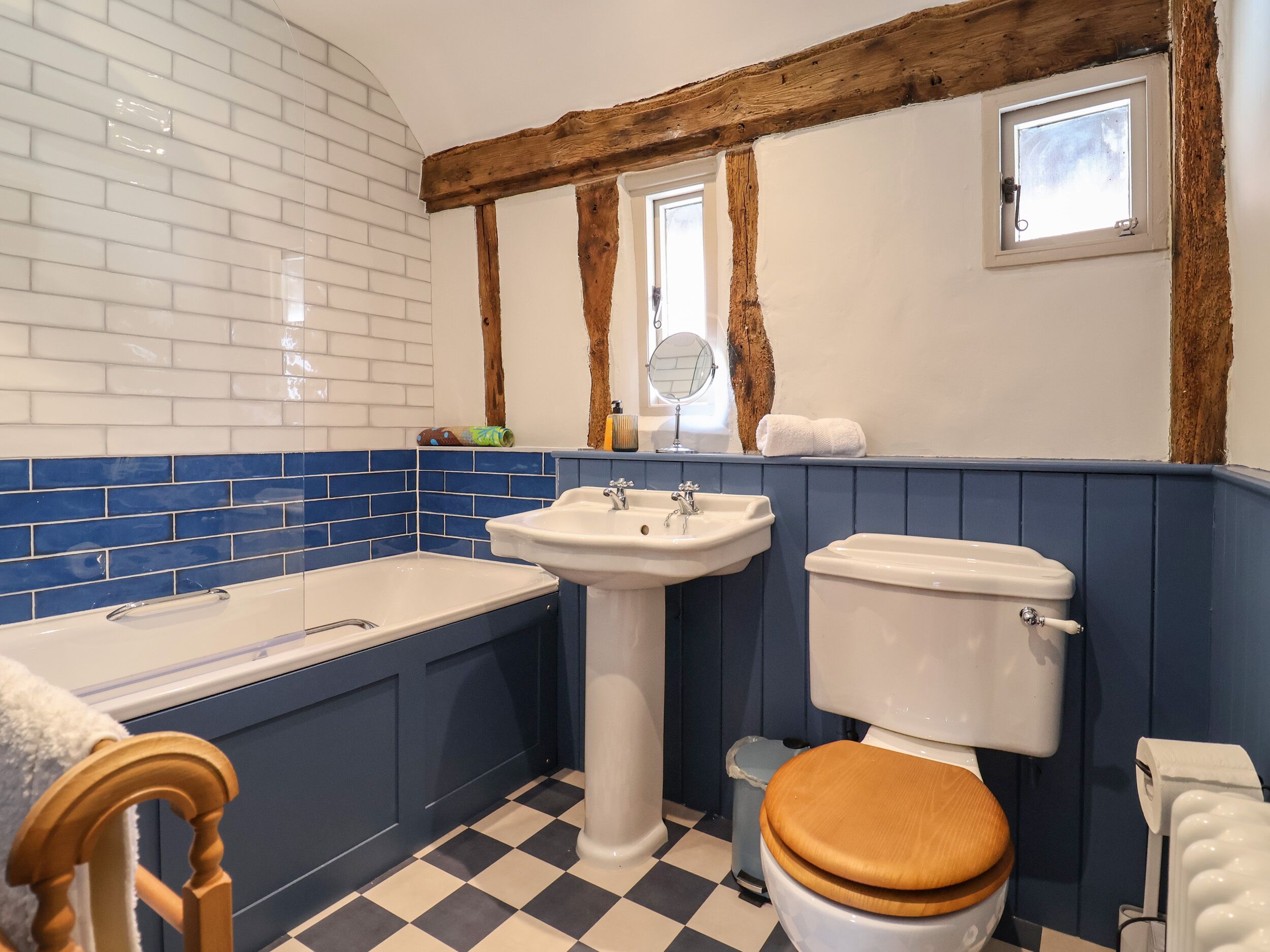 A bathroom with a bathtub, sink, toilet, and wooden chair.