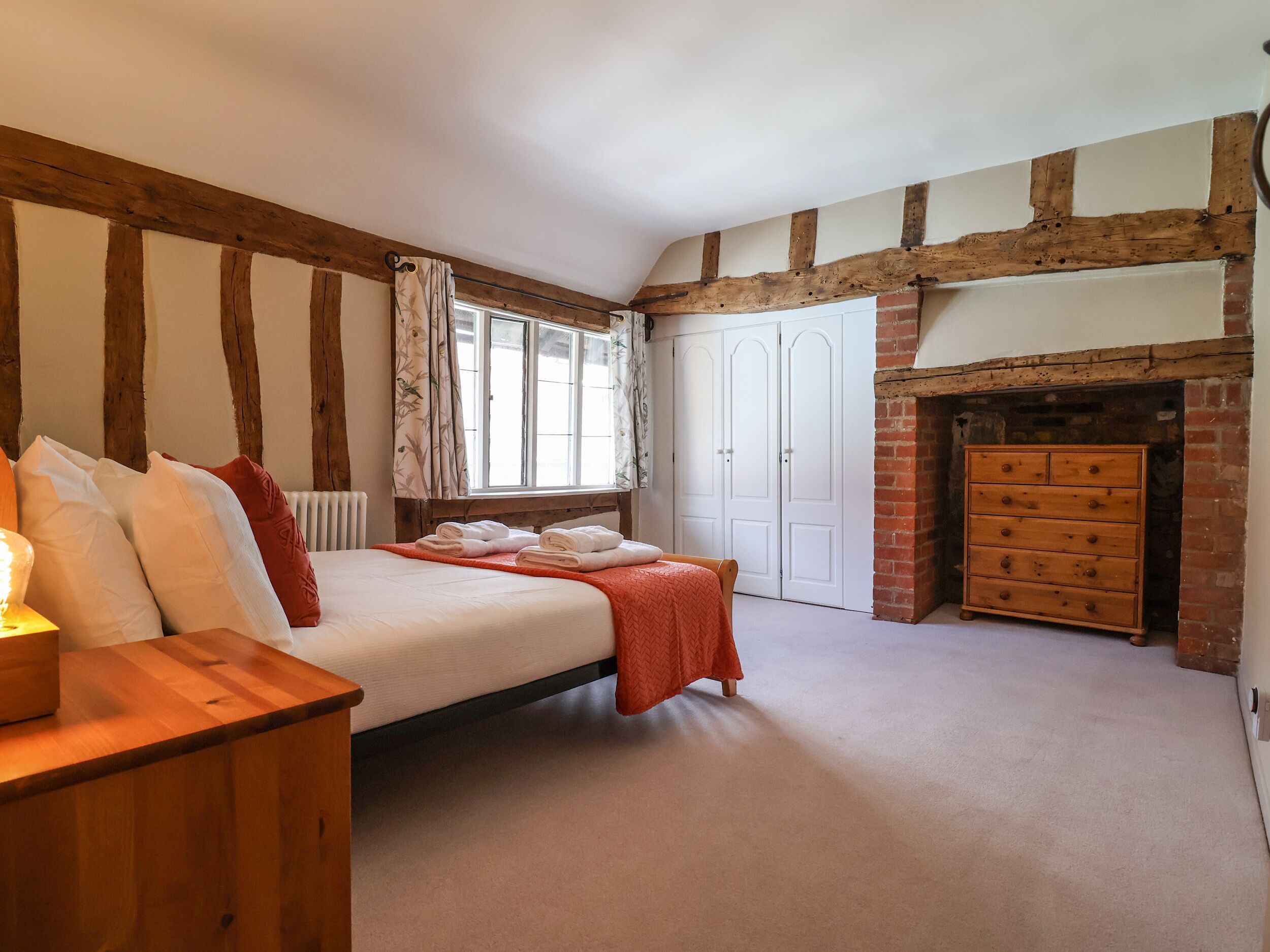Une chambre à coucher avec un lit en bois, une commode, une cheminée et une fenêtre avec des rideaux.