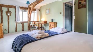 A bedroom with a large bed, a chair, a table with a lamp, and a door.