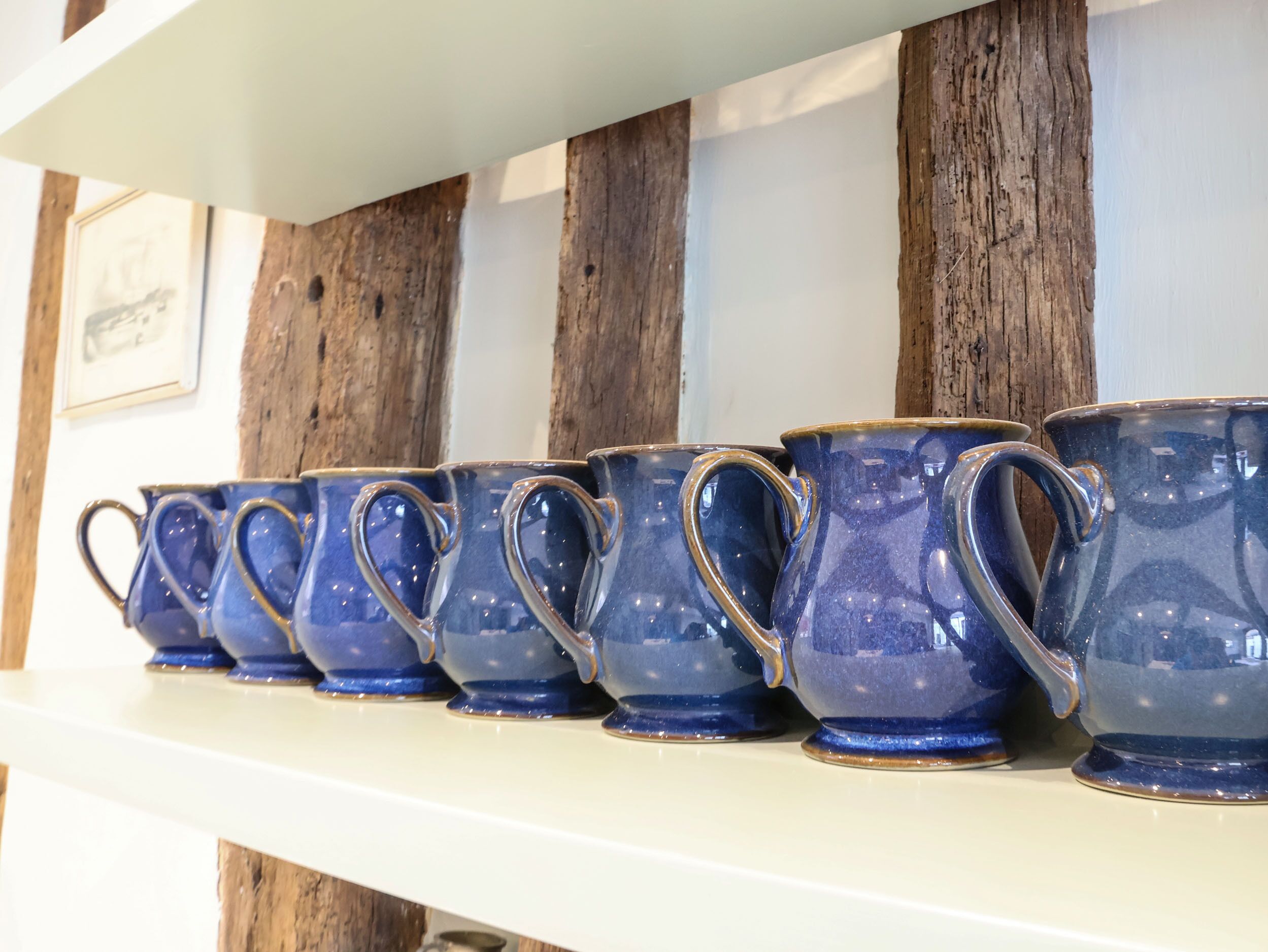 A row of blue ceramic mugs on a white shelf against a wooden wall.