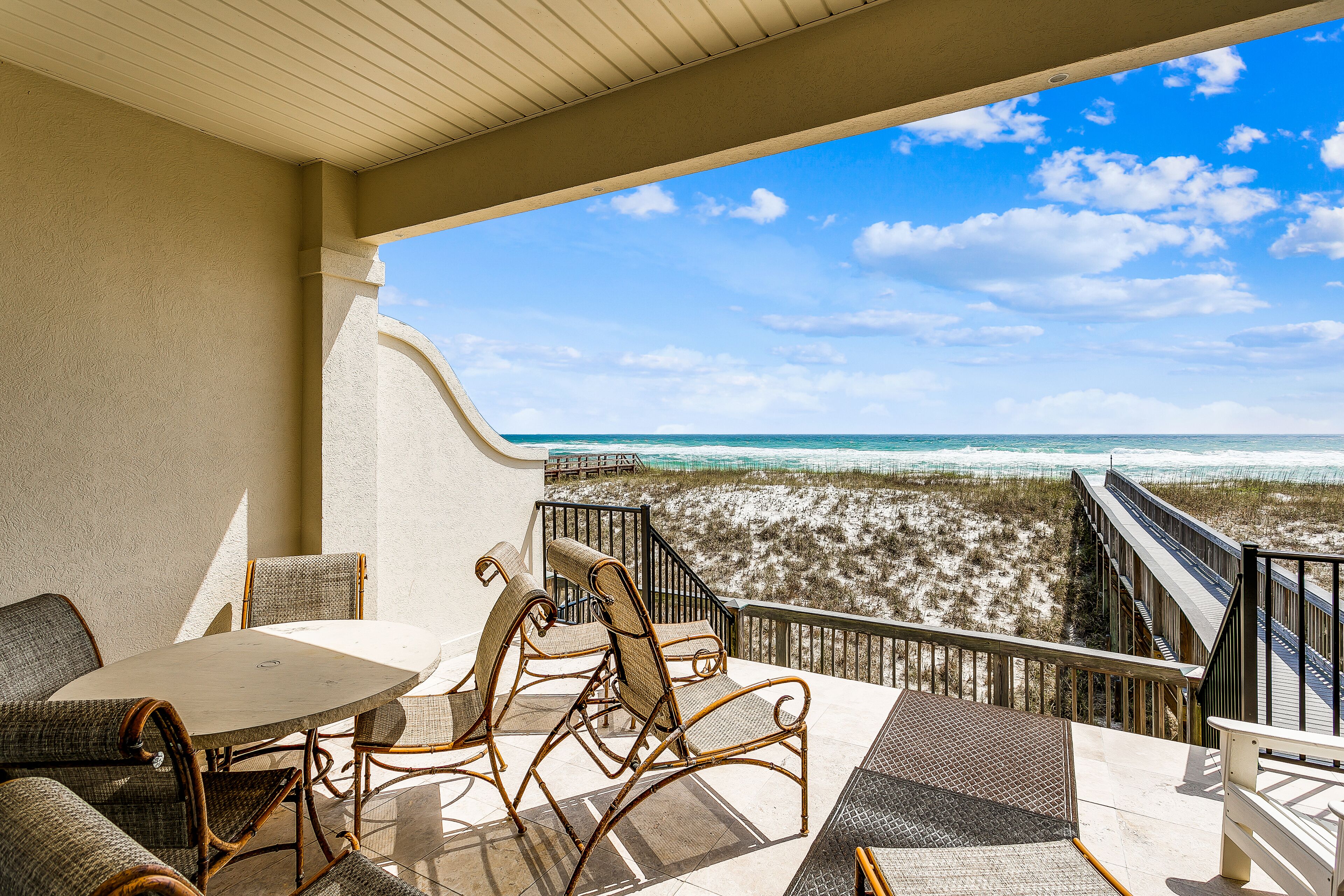 A balcony with wicker furniture, a view of the beach, and a wooden deck.