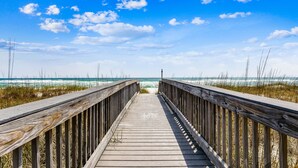A wooden boardwalk leading to a beach with clear skies and ocean waves.
