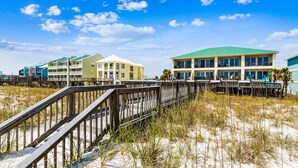 A beachfront hotel with multiple buildings, a wooden boardwalk, and sandy dunes.