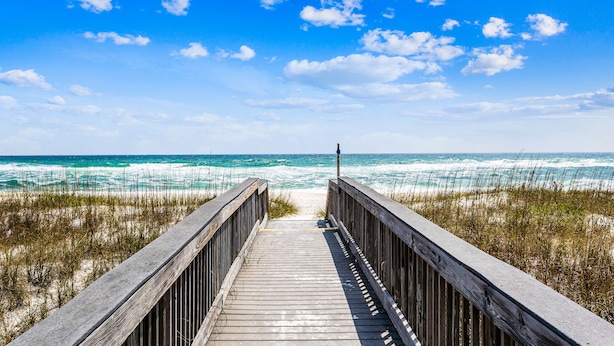 A wooden boardwalk leading to the beach with ocean waves in the background.