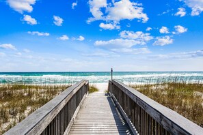 Une promenade en bois menant à la plage, avec les vagues de l’océan en arrière-plan.