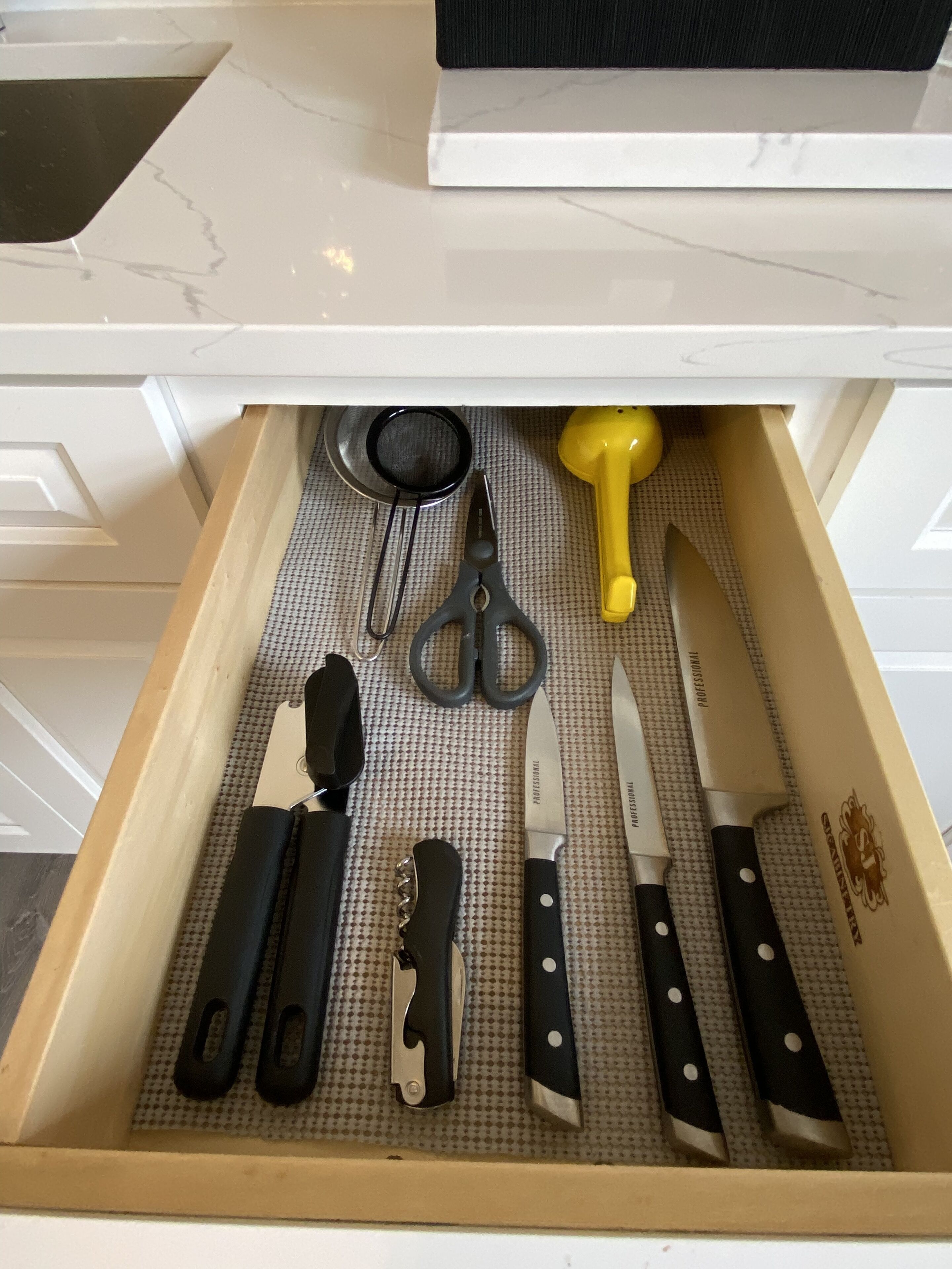 Un cajón con diversas herramientas de cocina, incluyendo tijeras, un mazo de goma amarillo y varios cuchillos.