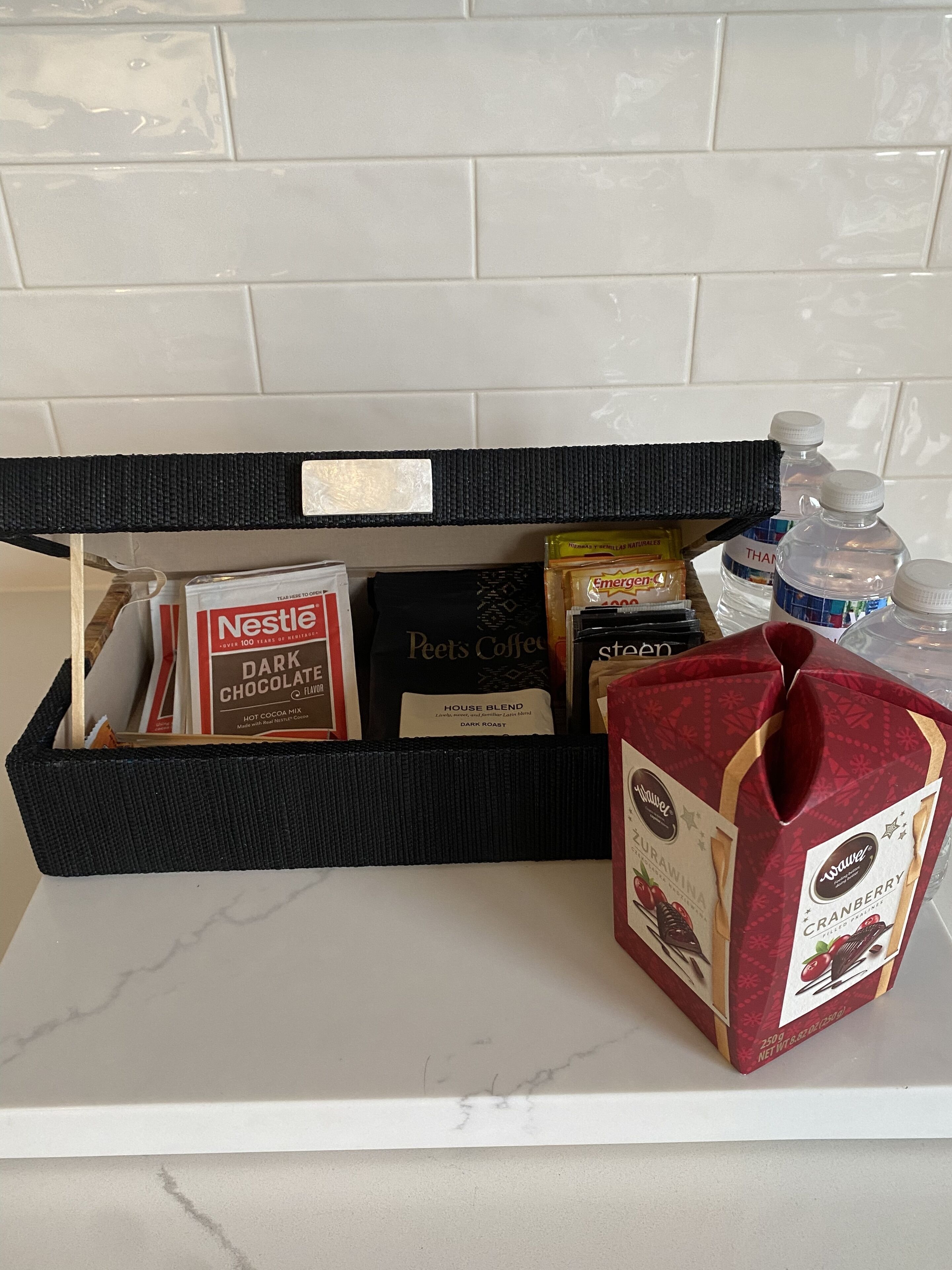 A kitchen counter with a black basket containing various food items, including a Nestle box, a Peet's Coffee bag, and a bag of Zucchini.