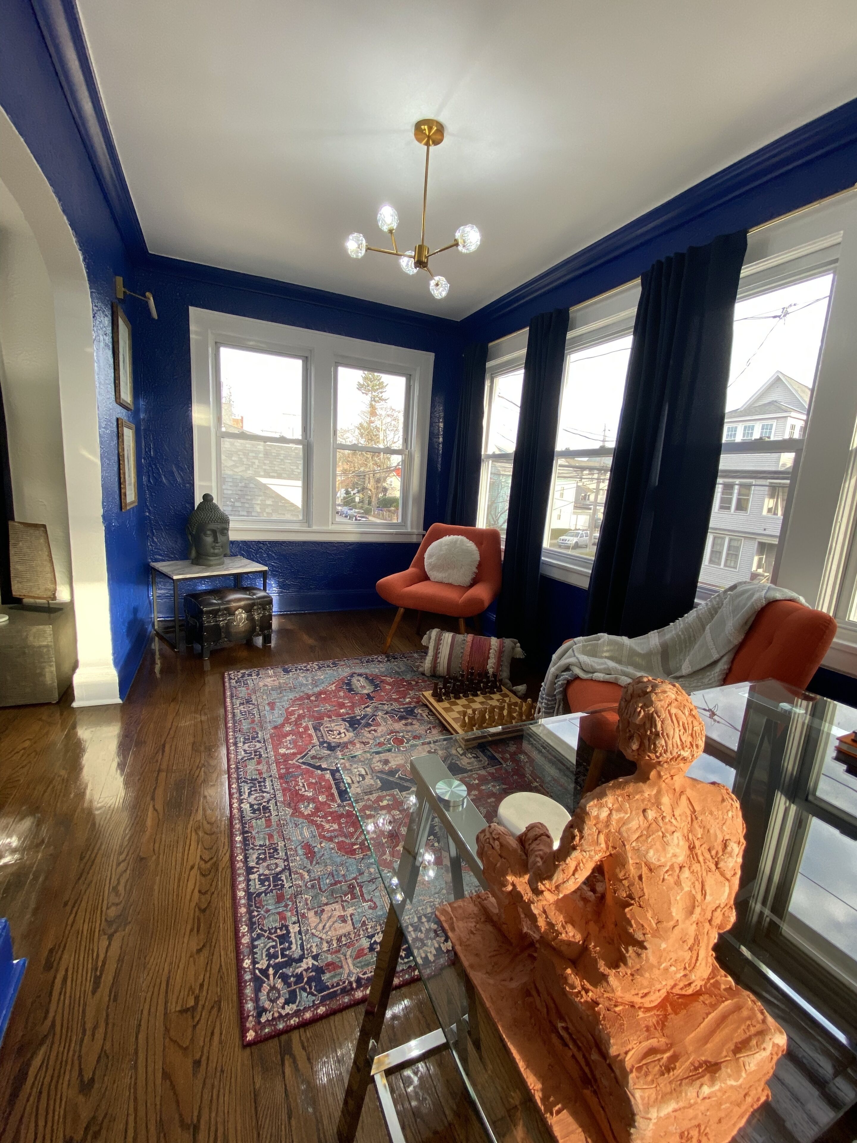 A living room with a blue wall, a wooden floor, a glass coffee table, a chessboard, and a statue.