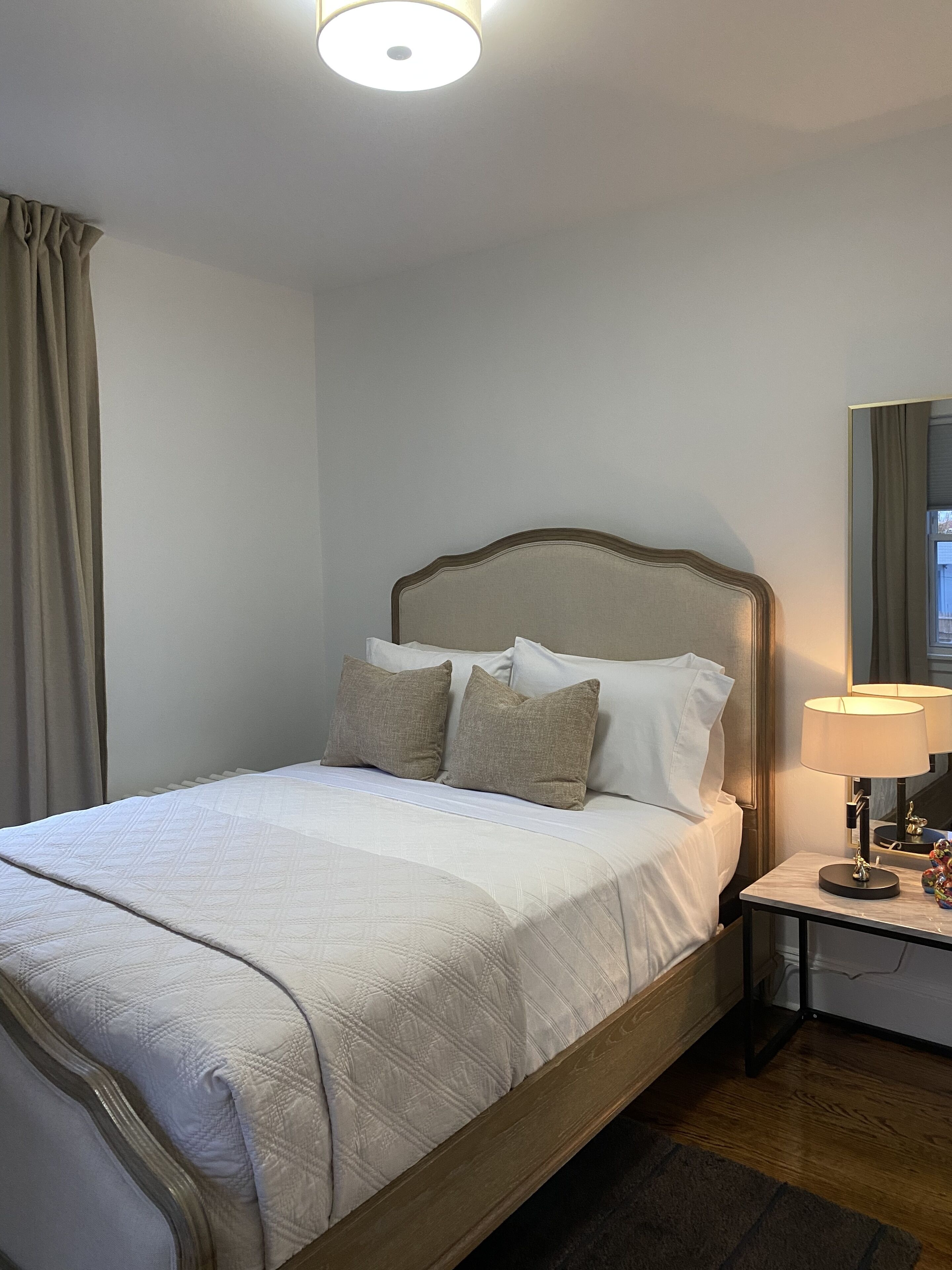 A neatly made bed with a wooden headboard, a bedside table with a lamp, and a mirror on the wall.