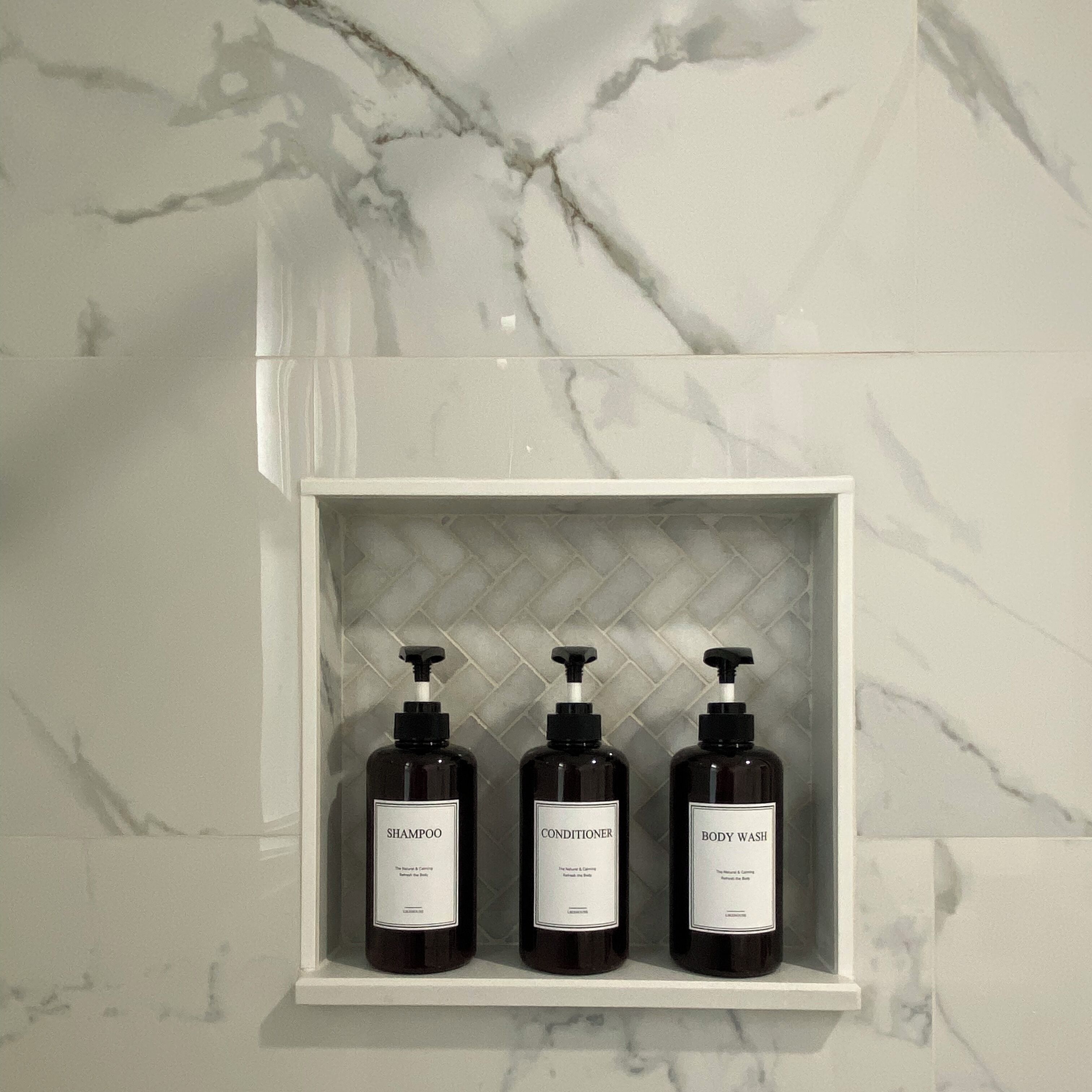 A bathroom shelf with three bottles of shampoo, conditioner, and body wash.