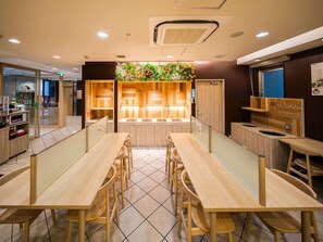 A restaurant interior with wooden tables and chairs, a counter with a menu, and a wall with a green plant display. - Super Hotel Osaka Chikatesu Tanimachi-4chome (Osaka)