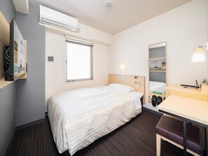 Habitación de hotel con una cama individual, un escritorio, una silla, un espejo, aire acondicionado instalado en la pared y una ventana.