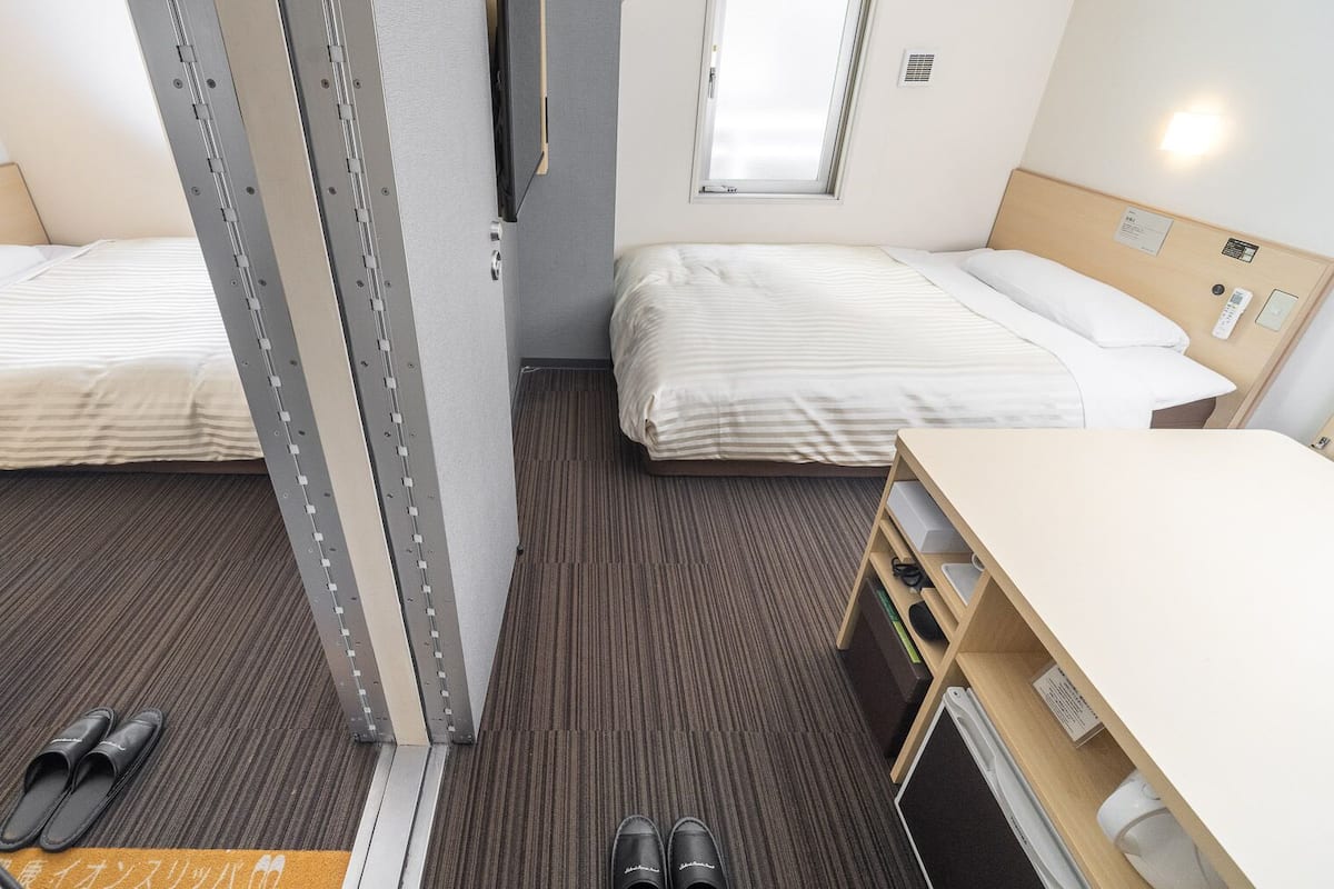 Habitació d'hotel amb dos llits, un escriptori i una cadira.
