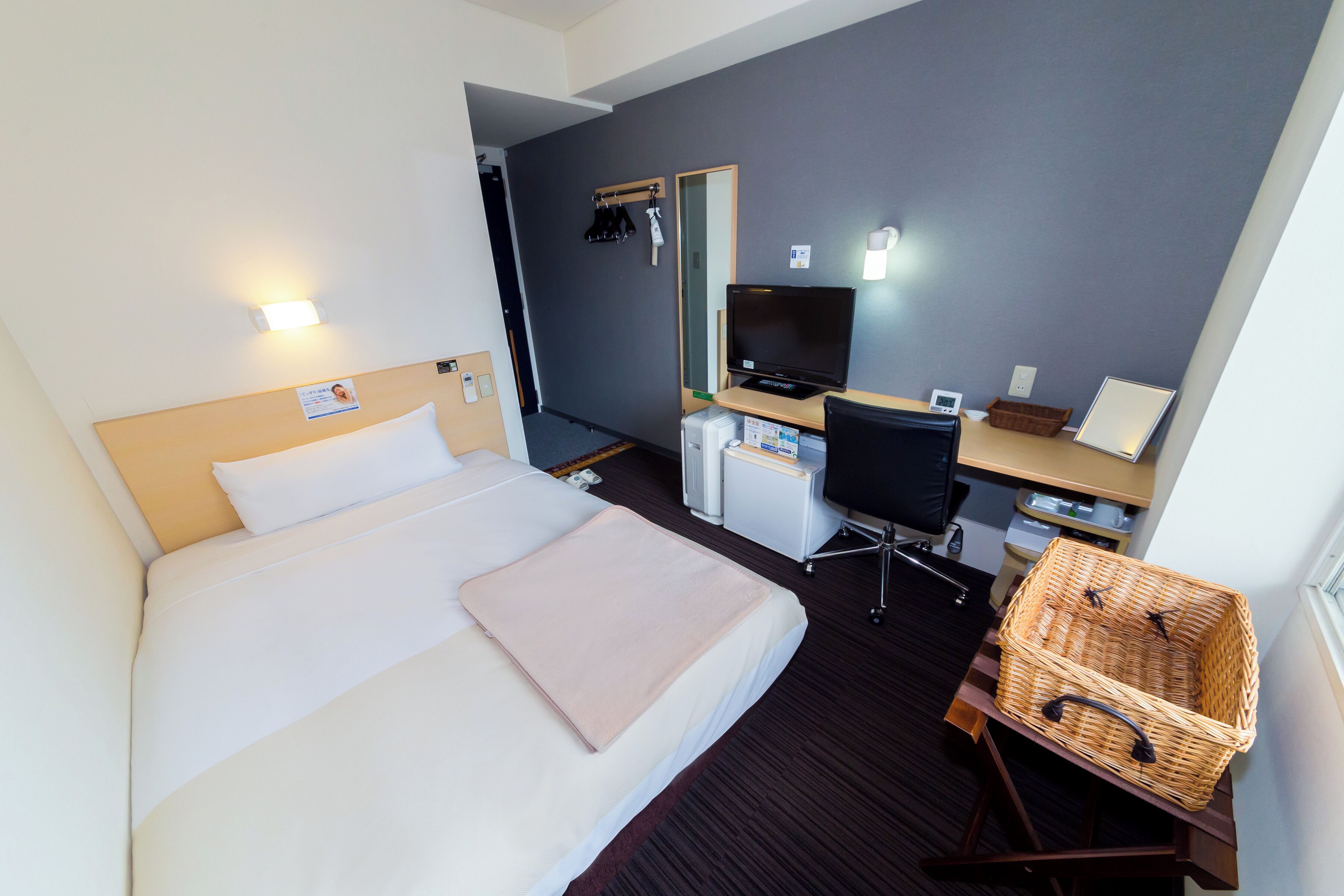 Ein Hotelzimmer mit Bett, Schreibtisch, Stuhl, Fernseher und einem Korb.