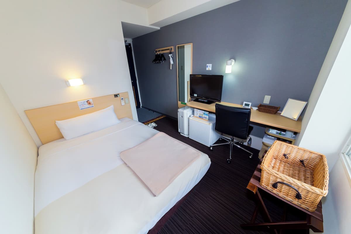 Habitació d'hotel amb llit, escriptori, cadira, televisió i cistella.