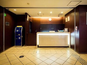 Zona de recepción de un hotel con mostrador, una máquina de autoservicio azul y un reloj en la pared.