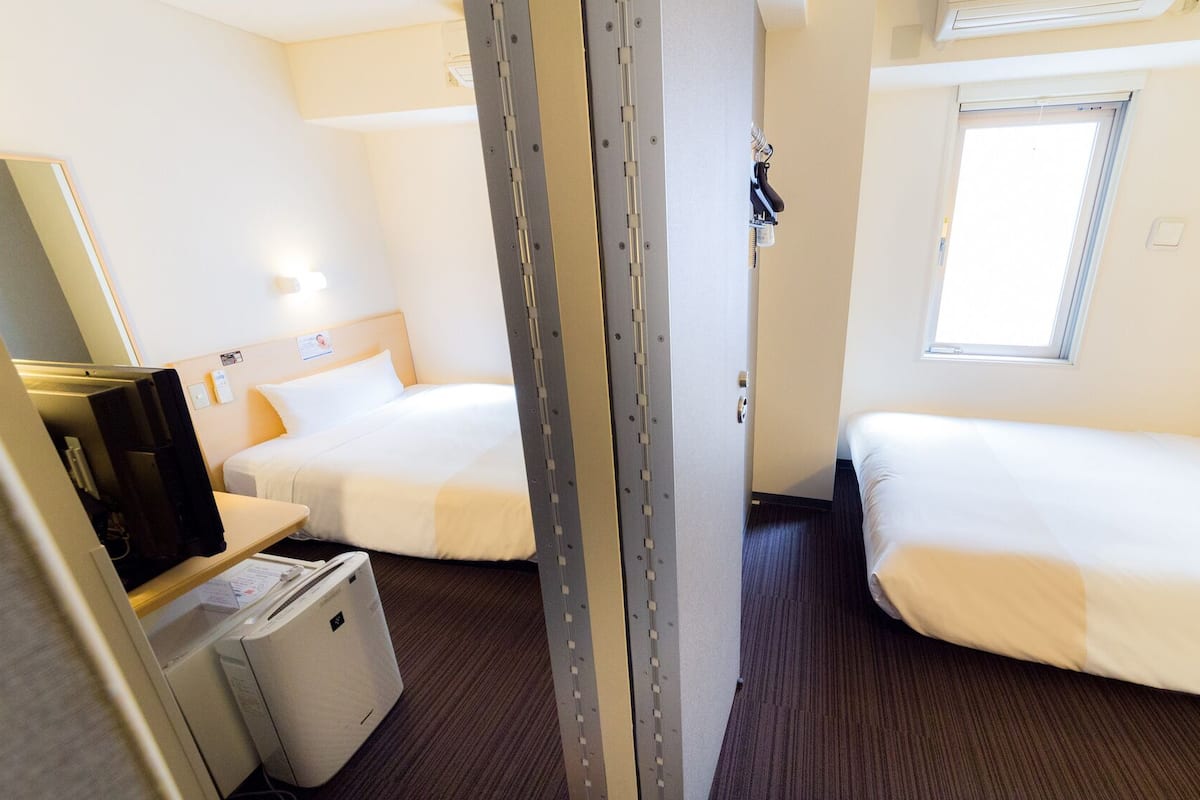 Habitació d'hotel amb dos llits, una taula de treball amb un ordinador, un petit calefactor i una finestra.