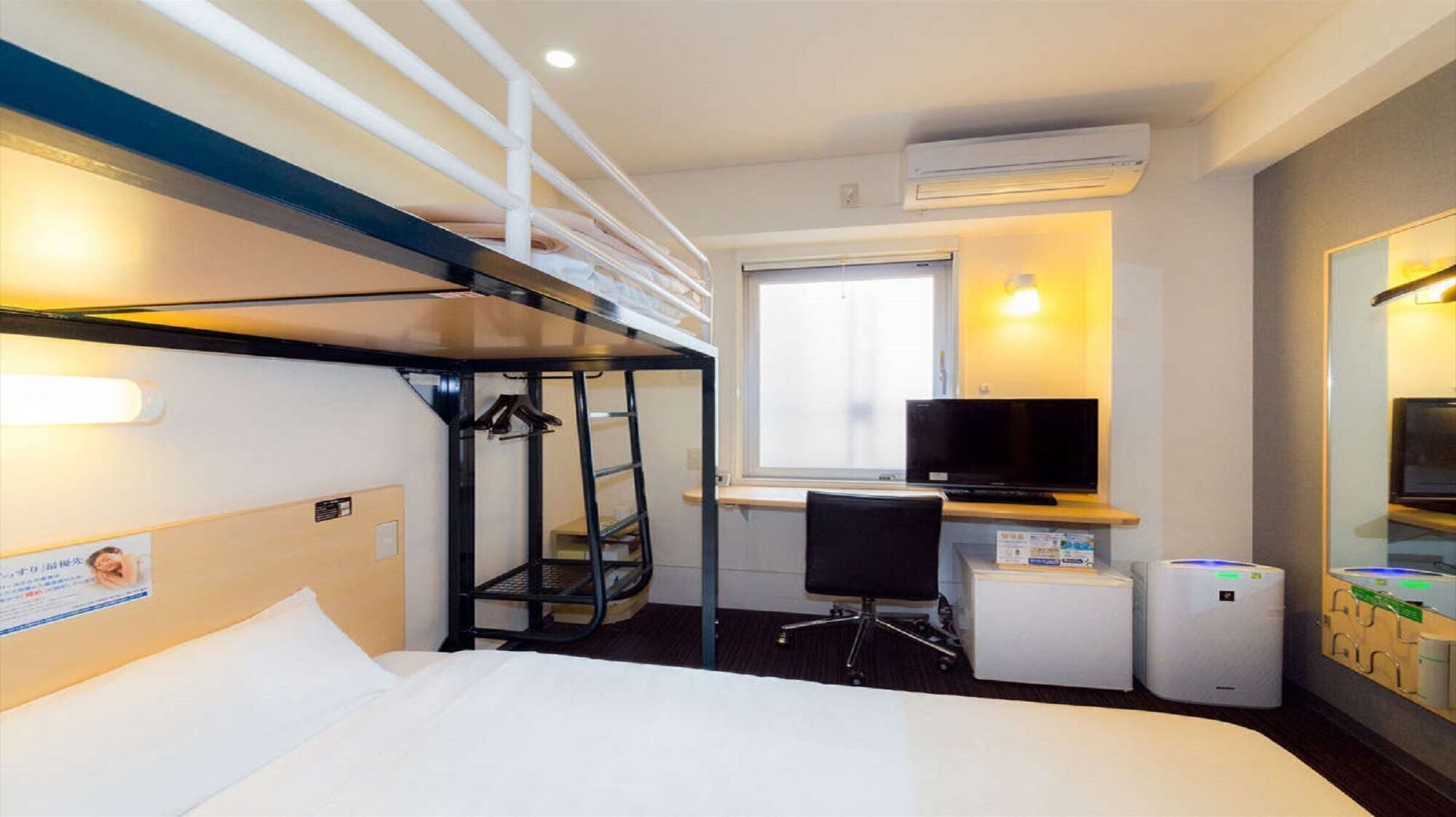 Ein Hotelzimmer mit Etagenbett, Schreibtisch inklusive Computer, Fernseher und kleinem Kühlschrank.